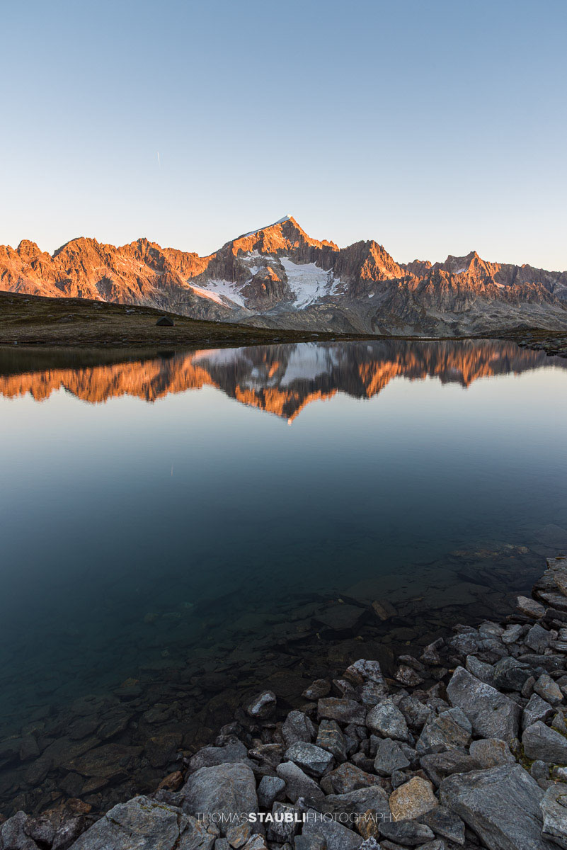 Die ersten Sonnenstrahlen treffen den Galenstock und spiegeln sich im Unteren Schwärziseeli bei den Stotzigen Firsten.