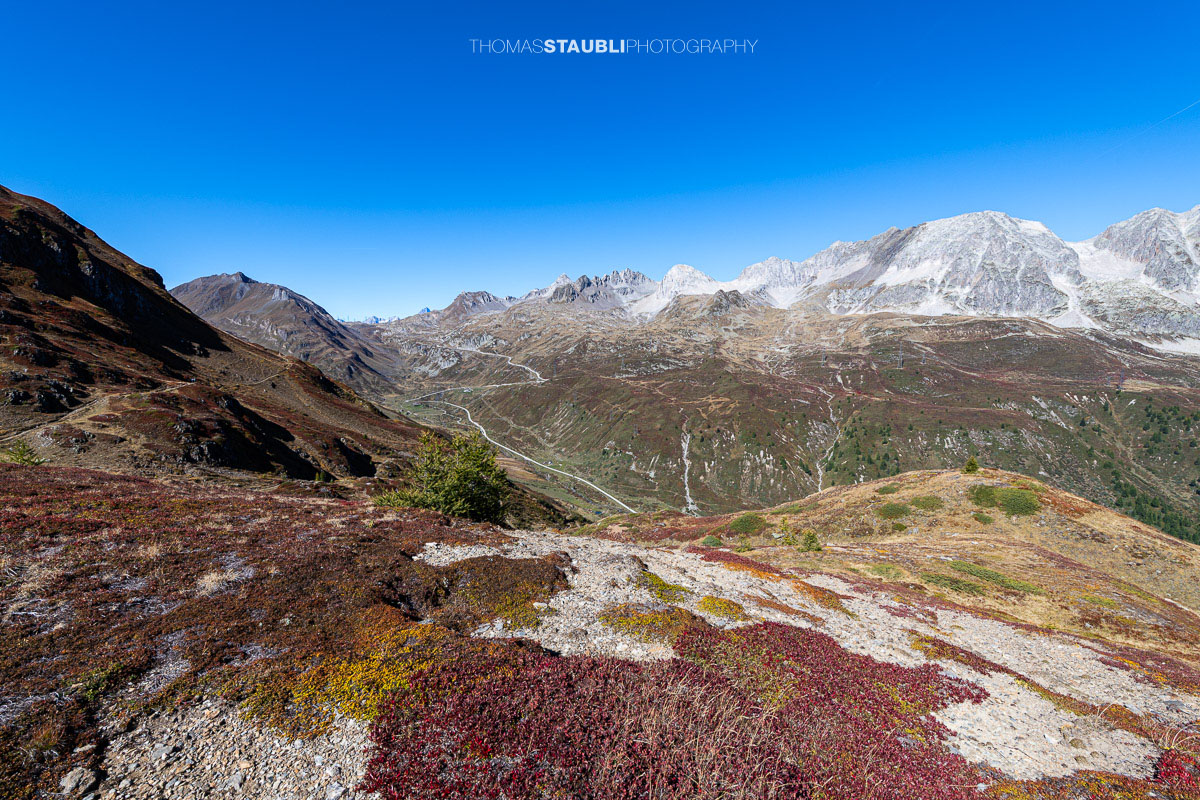 Blick vom Panoramaweg über das Val Bedretto mit herbstlich gefärbter Vegetation, weiten Berghängen und markanten Gipfeln.