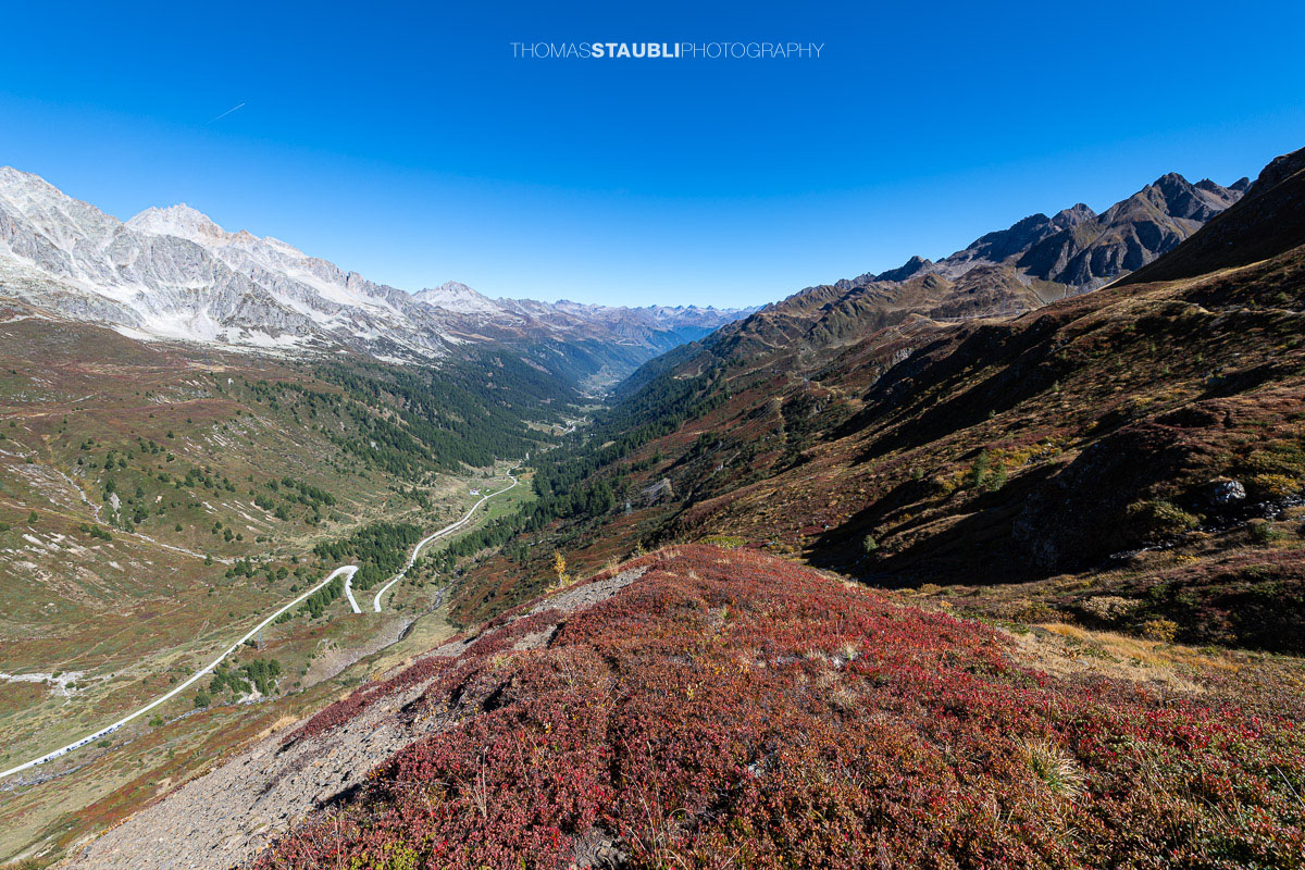 Blick vom Panoramaweg über das Val Bedretto mit herbstlich gefärbter Vegetation, weiten Berghängen und markanten Gipfeln.