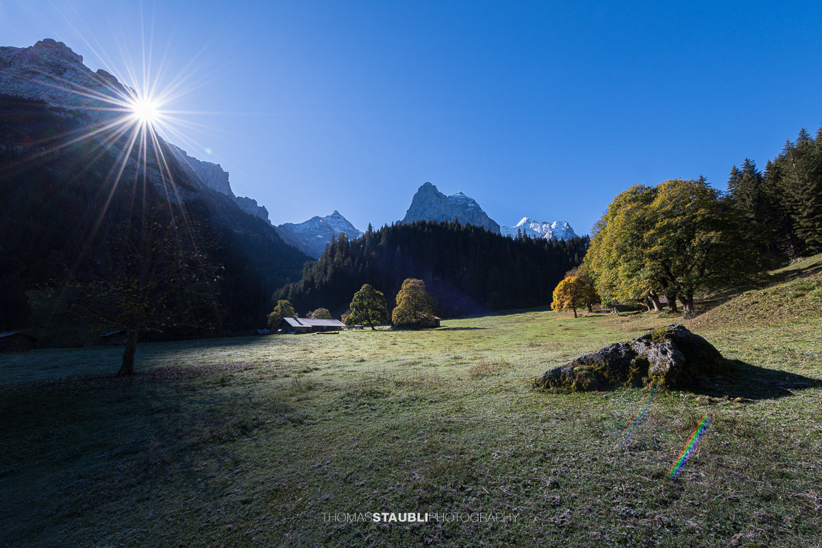 Herbstliche Morgenstimmung auf einer Wiese im Rychenbachtal mit dem Klein Wellhorn im Hintergrund und ersten Sonnenstrahlen über den Bergflanken.