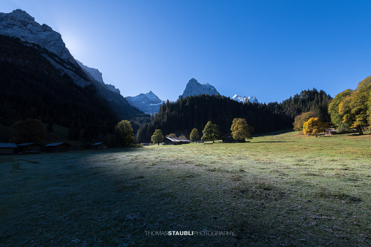 Herbstliche Morgenstimmung auf einer Wiese im Rychenbachtal mit dem Klein Wellhorn im Hintergrund und ersten Sonnenstrahlen über den Bergflanken.