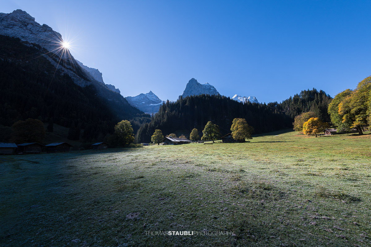 Herbstliche Morgenstimmung auf einer Wiese im Rychenbachtal mit dem Klein Wellhorn im Hintergrund und ersten Sonnenstrahlen über den Bergflanken.