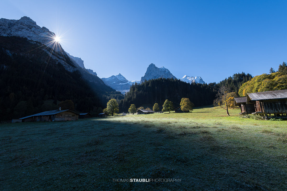 Herbstliche Morgenstimmung auf einer Wiese im Rychenbachtal mit dem Klein Wellhorn im Hintergrund und ersten Sonnenstrahlen über den Bergflanken.