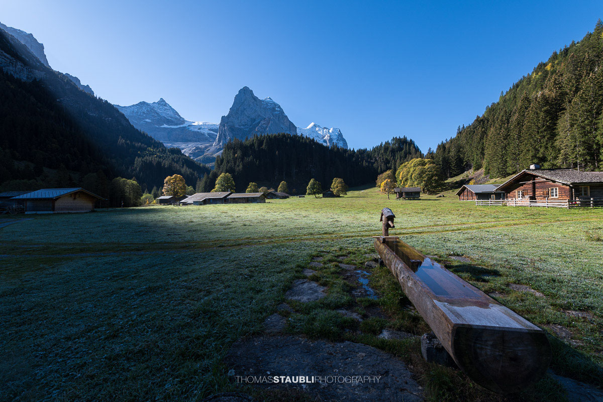 Herbstliche Morgenstimmung auf einer Wiese im Rychenbachtal mit dem Klein Wellhorn im Hintergrund und ersten Sonnenstrahlen über den Bergflanken.
